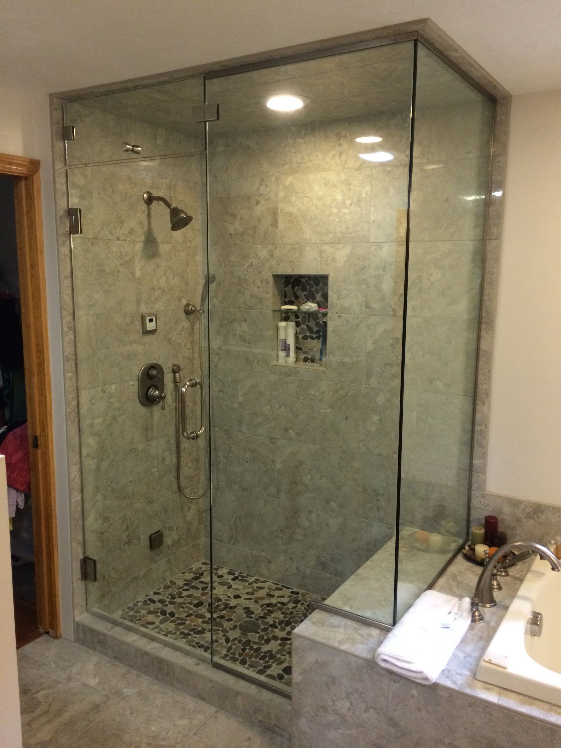 Glass-enclosed shower with gray tiled walls and pebble floor. Built-in seat and toiletries niche.