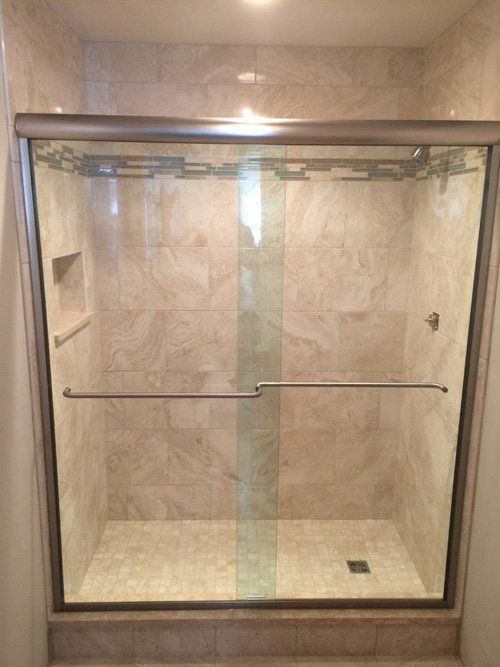 Shower with glass doors, tiled walls and floor, and chrome fixtures.