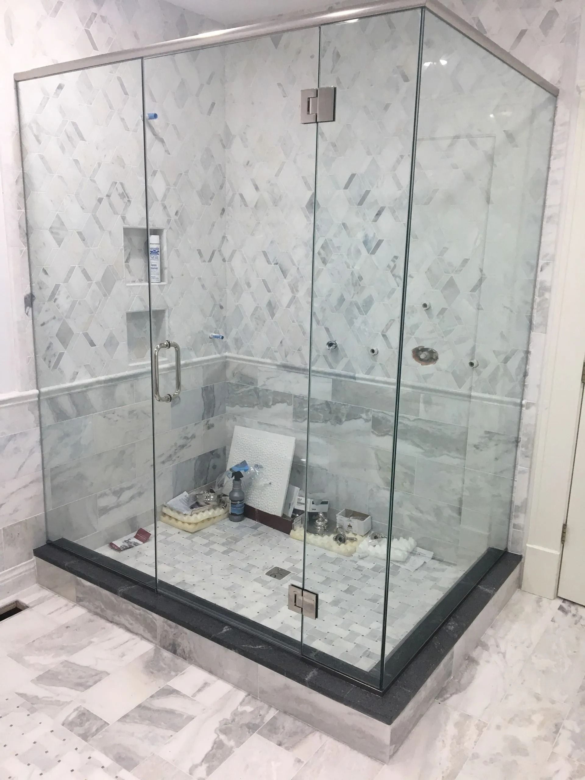 Glass shower enclosure in a bathroom with marble tile and dark trim.