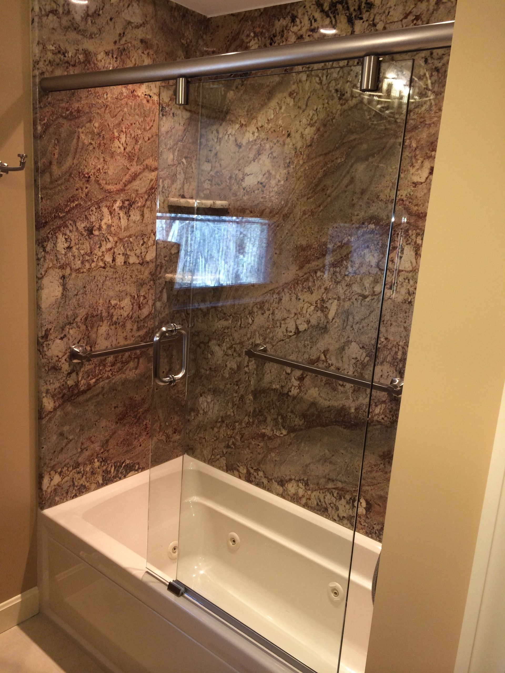 Bathtub enclosed in glass, with brown marble-like walls and a recessed shelf.