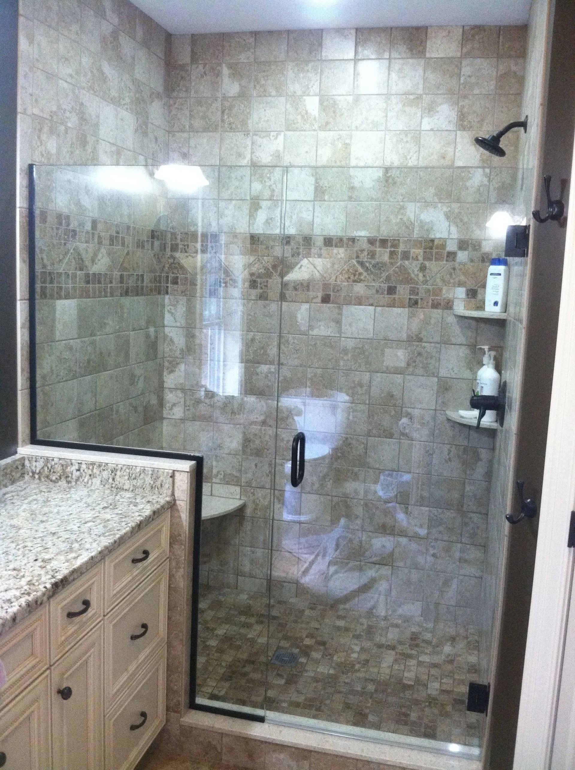Shower with beige tile and glass door, granite vanity, and dark fixtures.