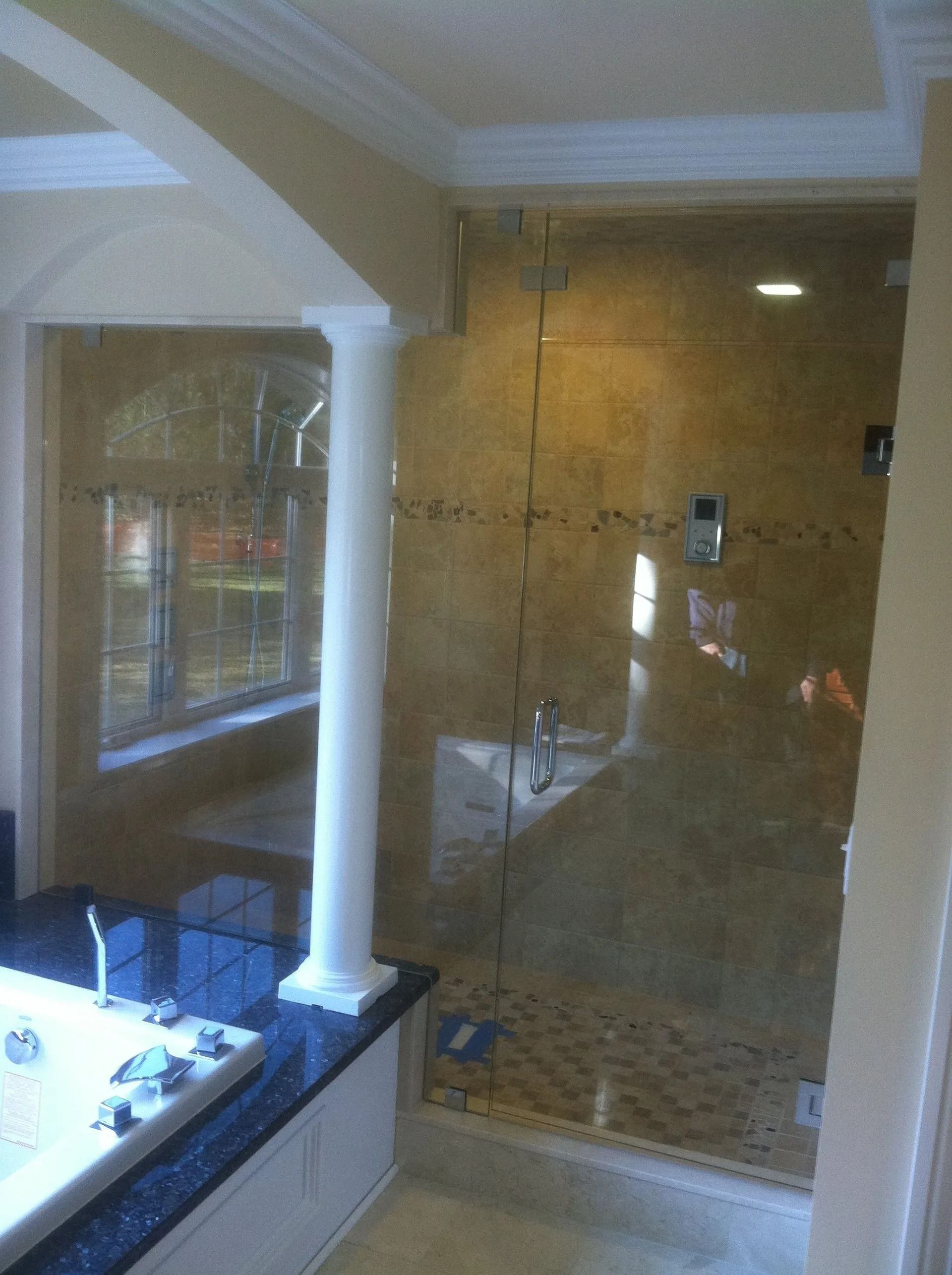 Bathroom with a glass shower enclosure and a white column. Light brown tile walls.