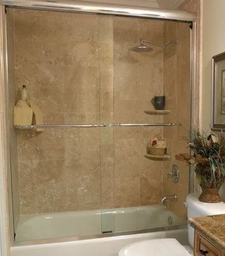 Shower with tan tiled walls, glass doors, and a built-in shelf.