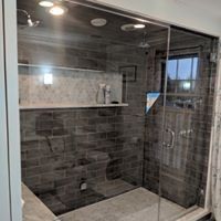 Glass-enclosed shower with gray tiled walls and floor, a white shelf, and a window.