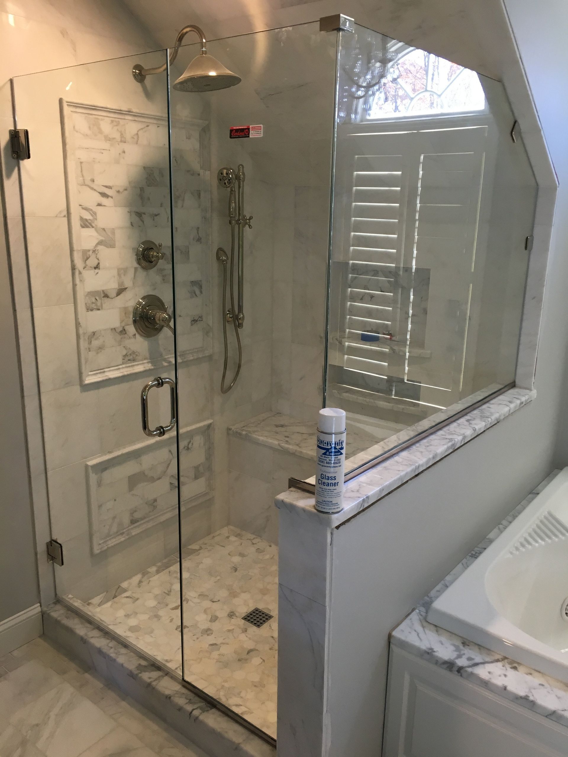 Glass shower enclosure with marble tile, silver fixtures, and a bench.