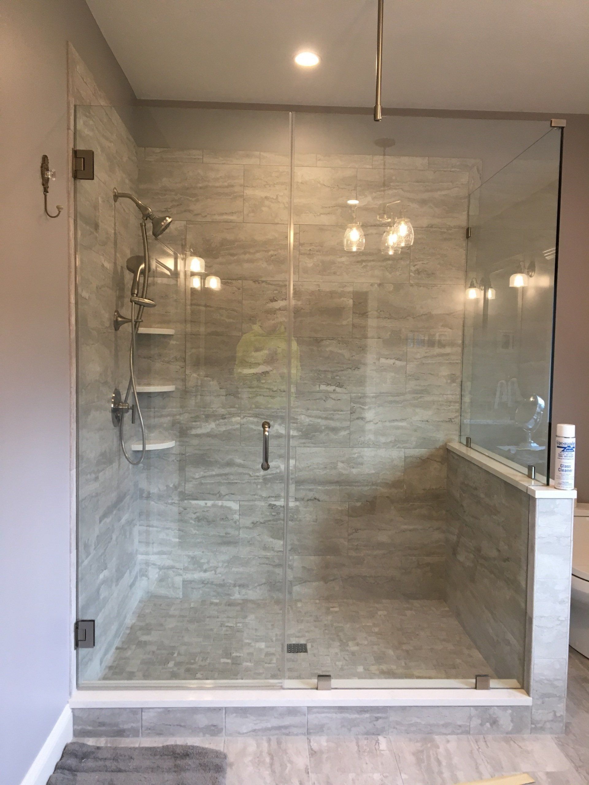 Glass-enclosed shower with gray tiled walls and floor, stainless steel fixtures, and a clear glass door.