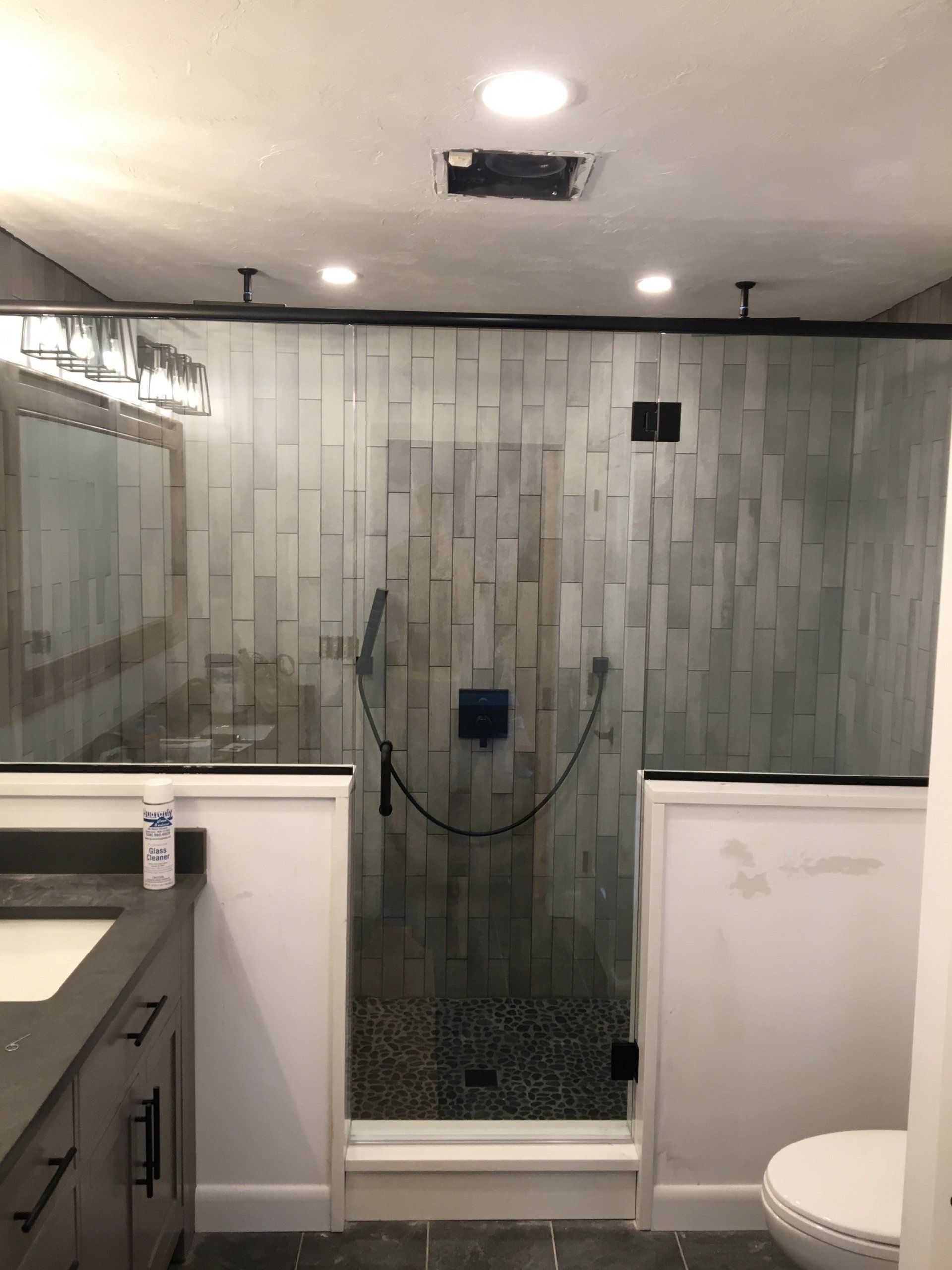Bathroom with glass shower, textured gray tile, dark hardware, and a black showerhead.