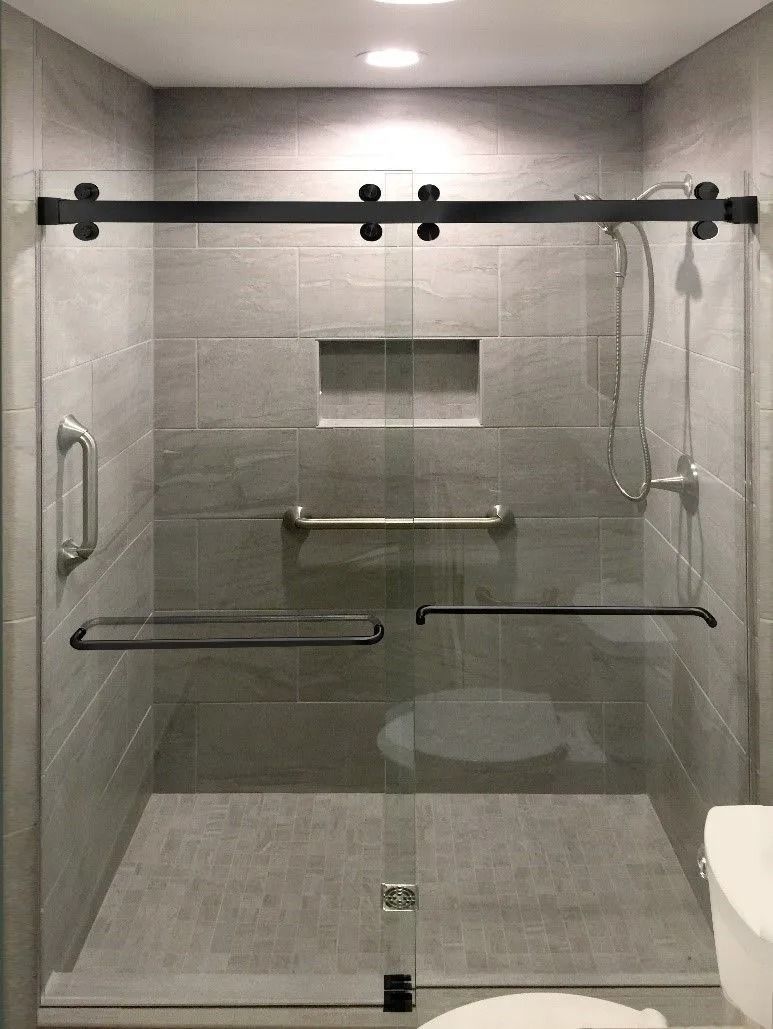 Modern shower stall with gray tiled walls, glass doors, and black hardware; includes grab bars.