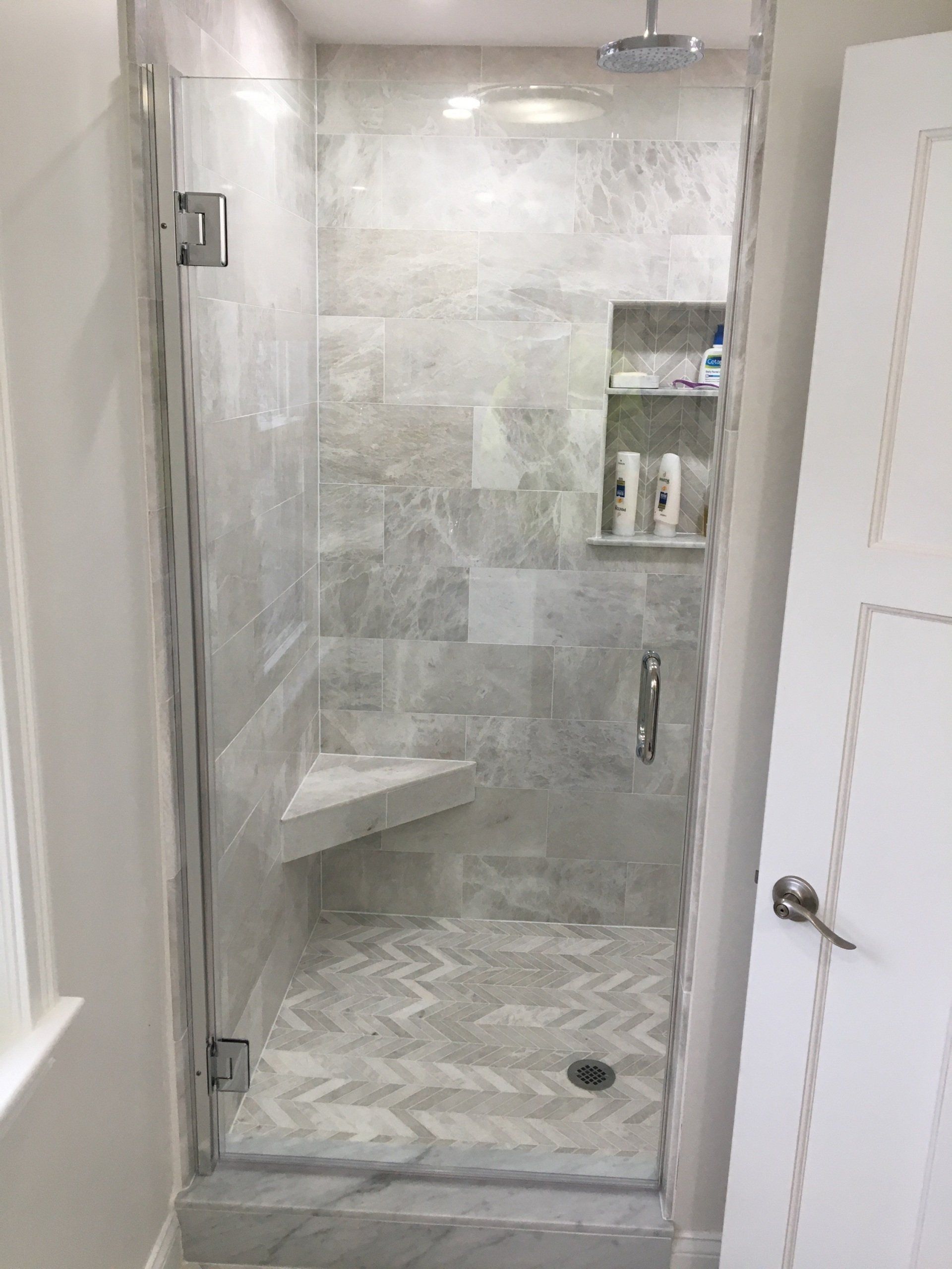 Glass shower with light gray marble tile and a built-in bench.