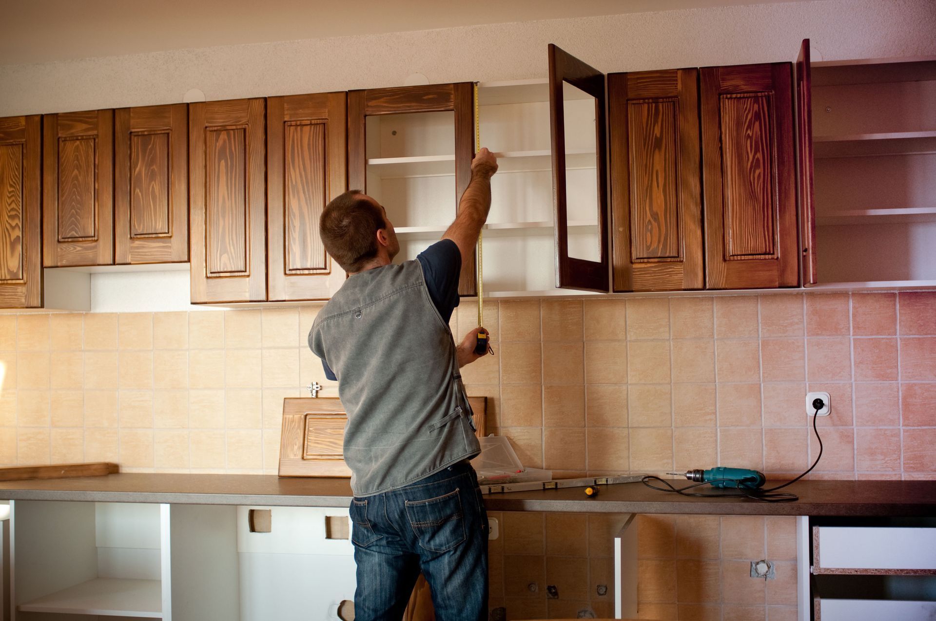 Man measuring a kitchen cabinet's interior during a renovation.