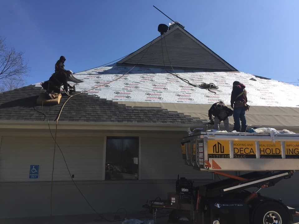 Roofers replacing shingles on a building with a blue sky background. Construction lift in use.