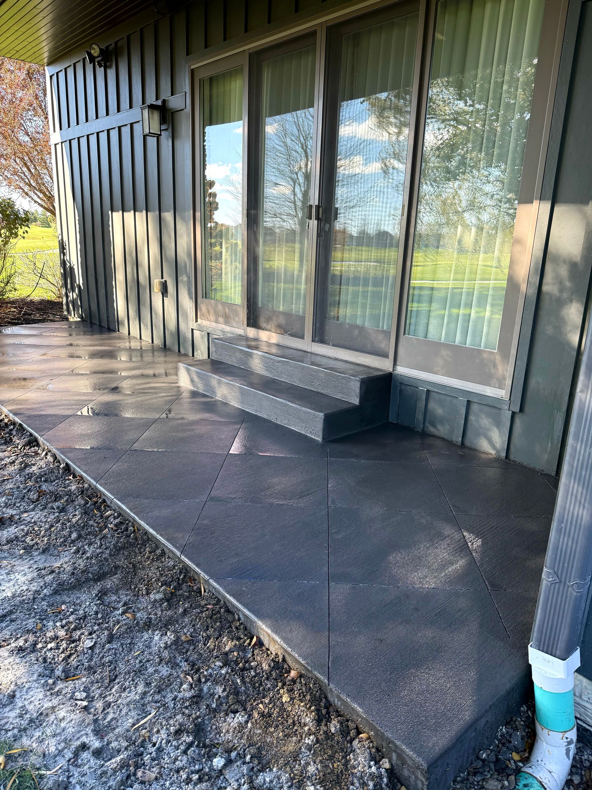 Dark concrete patio with steps leading to a sliding glass door. The house exterior is dark green.