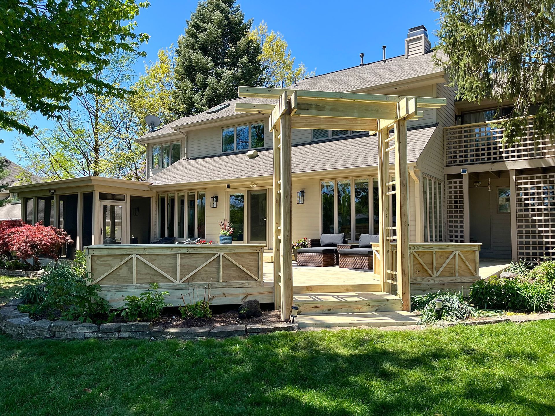 A backyard deck with wooden structures, a house, and a green lawn on a sunny day.