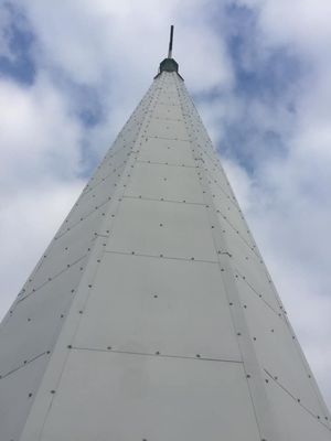 White, tapered tower against a cloudy sky, with rivets and a pointed top.