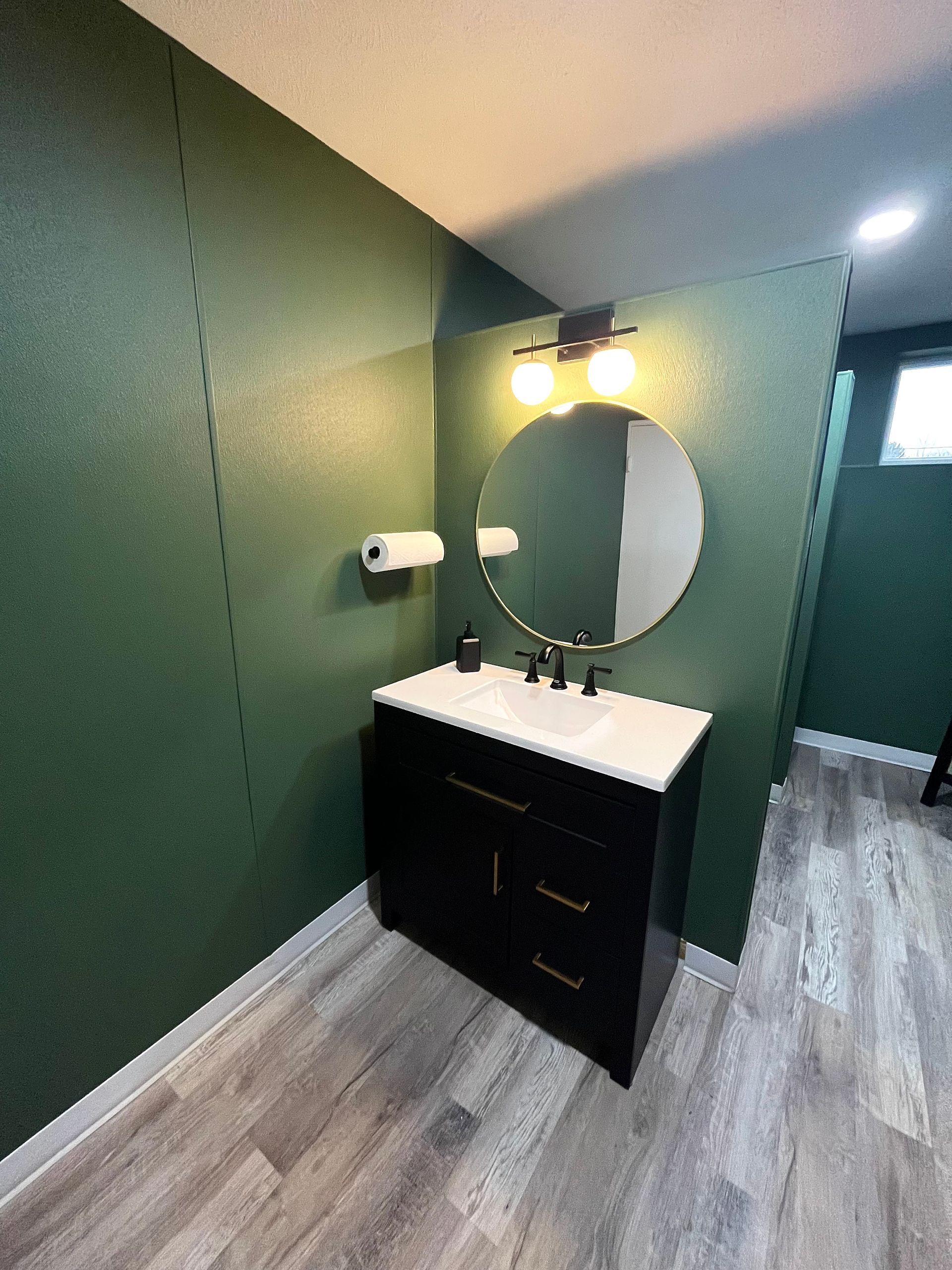 Small bathroom with a black vanity, round mirror, and green walls.