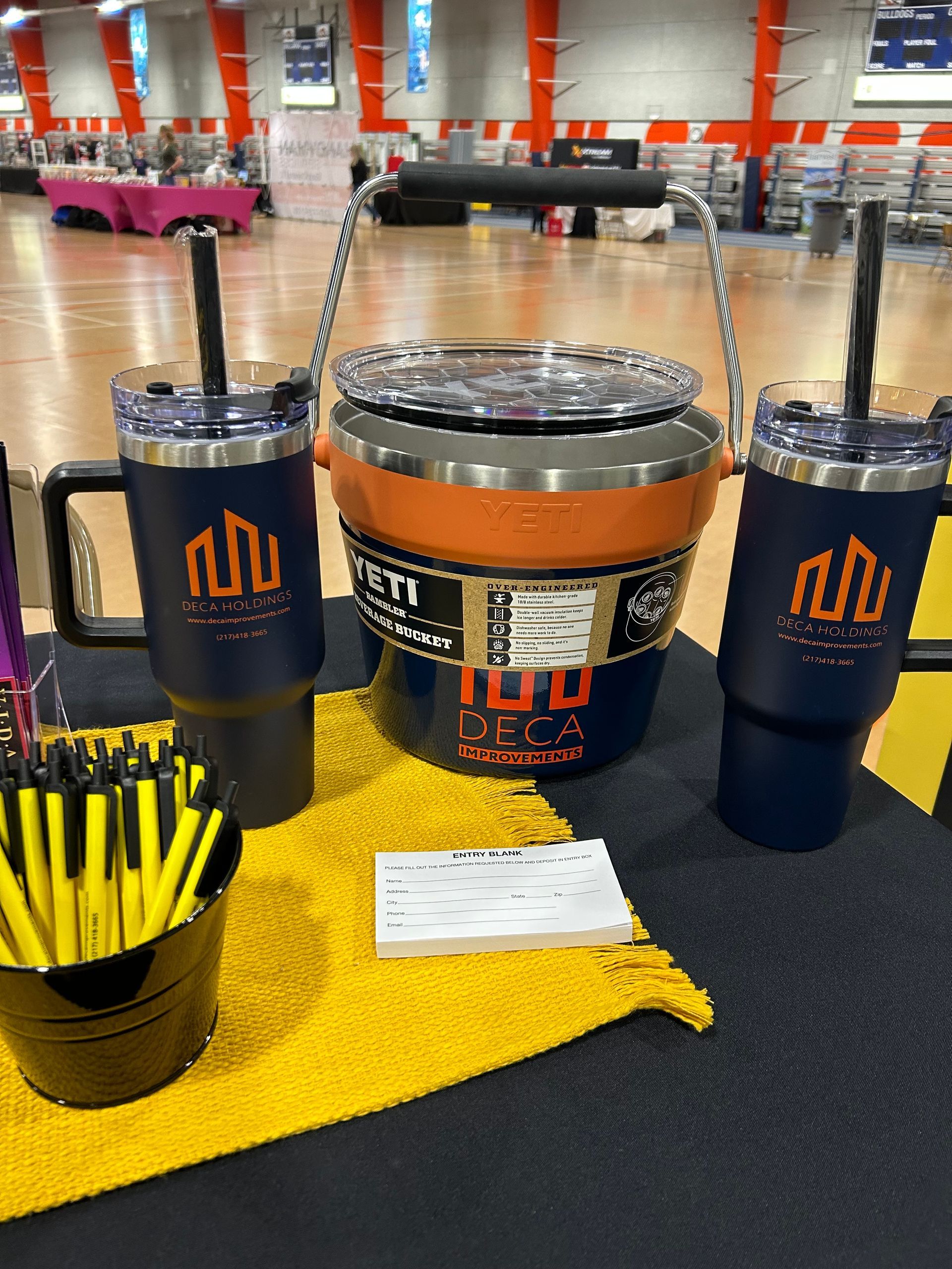 Yeti cooler with two matching navy mugs with logo and yellow pens in bucket.