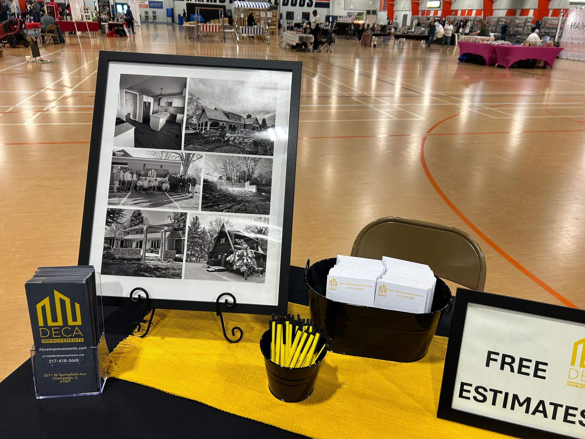 A home remodeling booth at a convention. Display includes a framed photo collage, business cards, and a sign for free estimates.