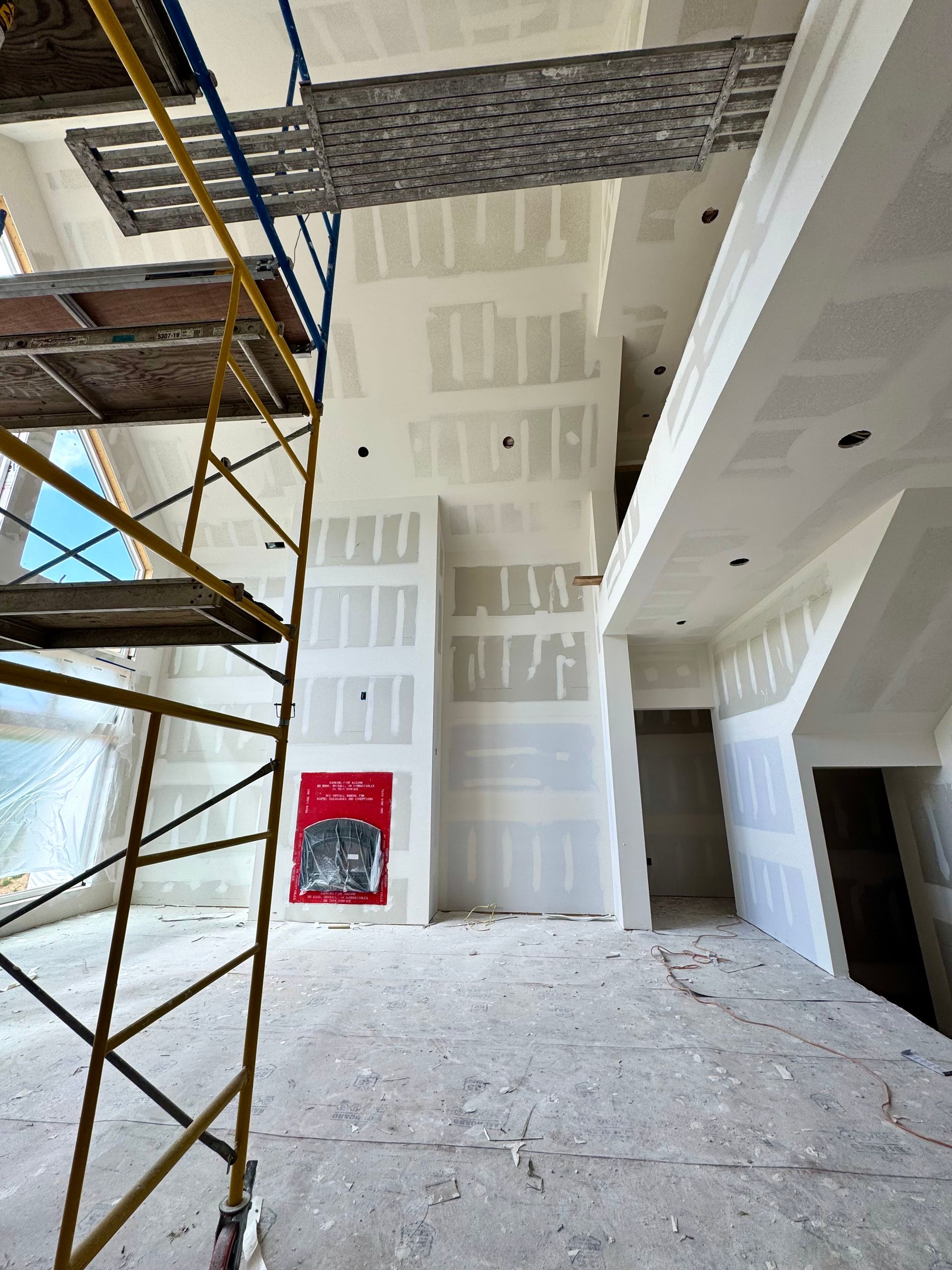 Interior under construction: drywall, scaffolding, firebox, neutral colors, open space.