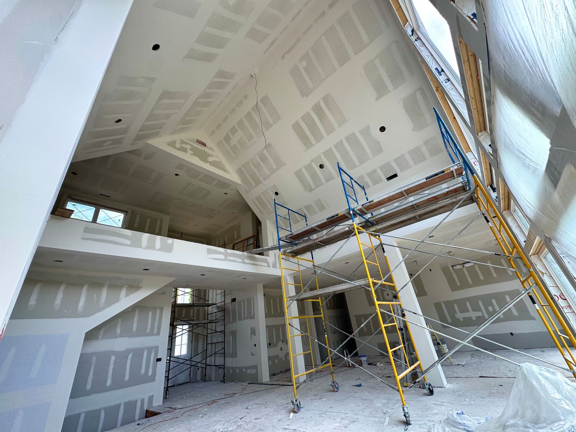 Interior view of house under construction; drywall installation, scaffolding present.