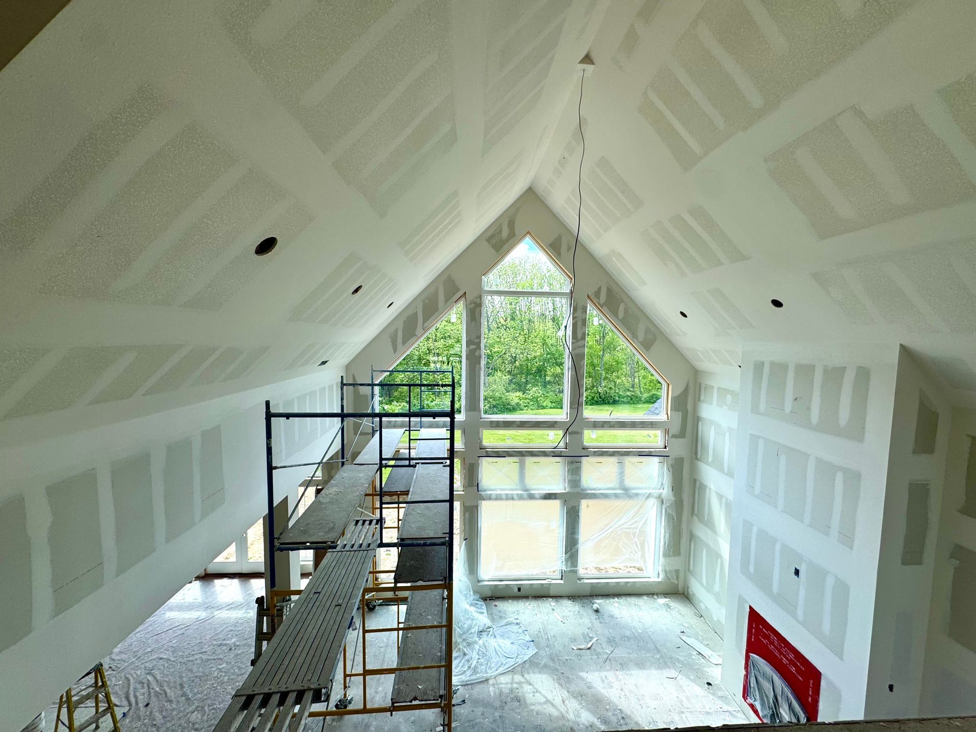 Interior of a house under construction with drywall installed. Scaffolding is positioned below a large window.