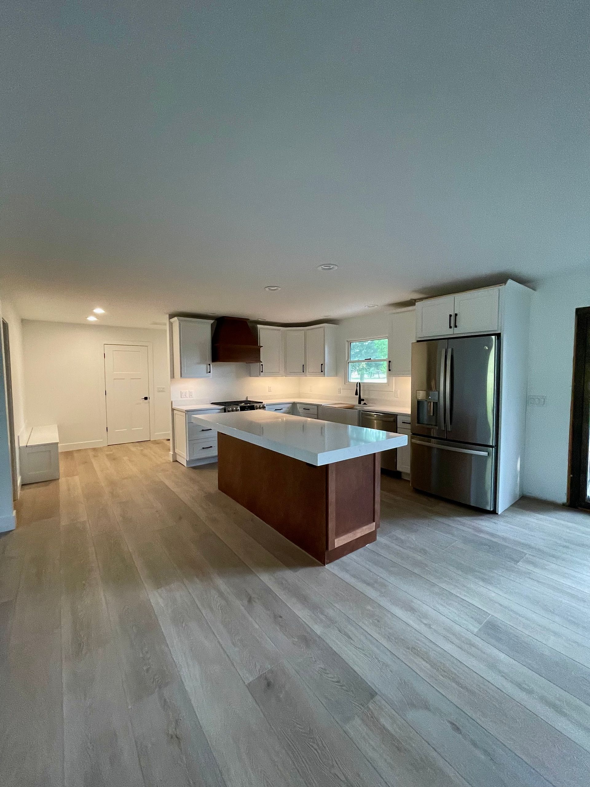 Spacious kitchen with wood floors and white cabinets. Island with dark wood base. Stainless steel refrigerator.
