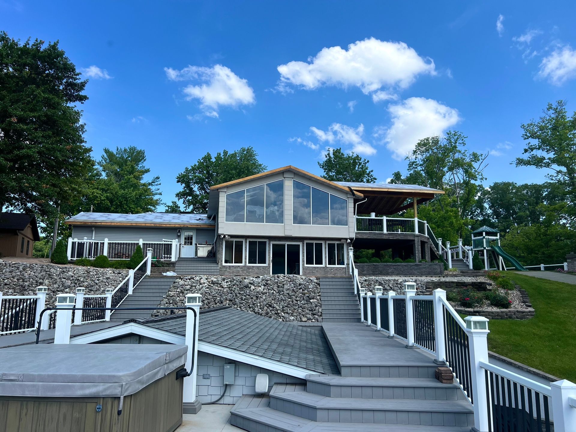 Lake house with multiple decks and a large glass-fronted section; blue sky overhead.