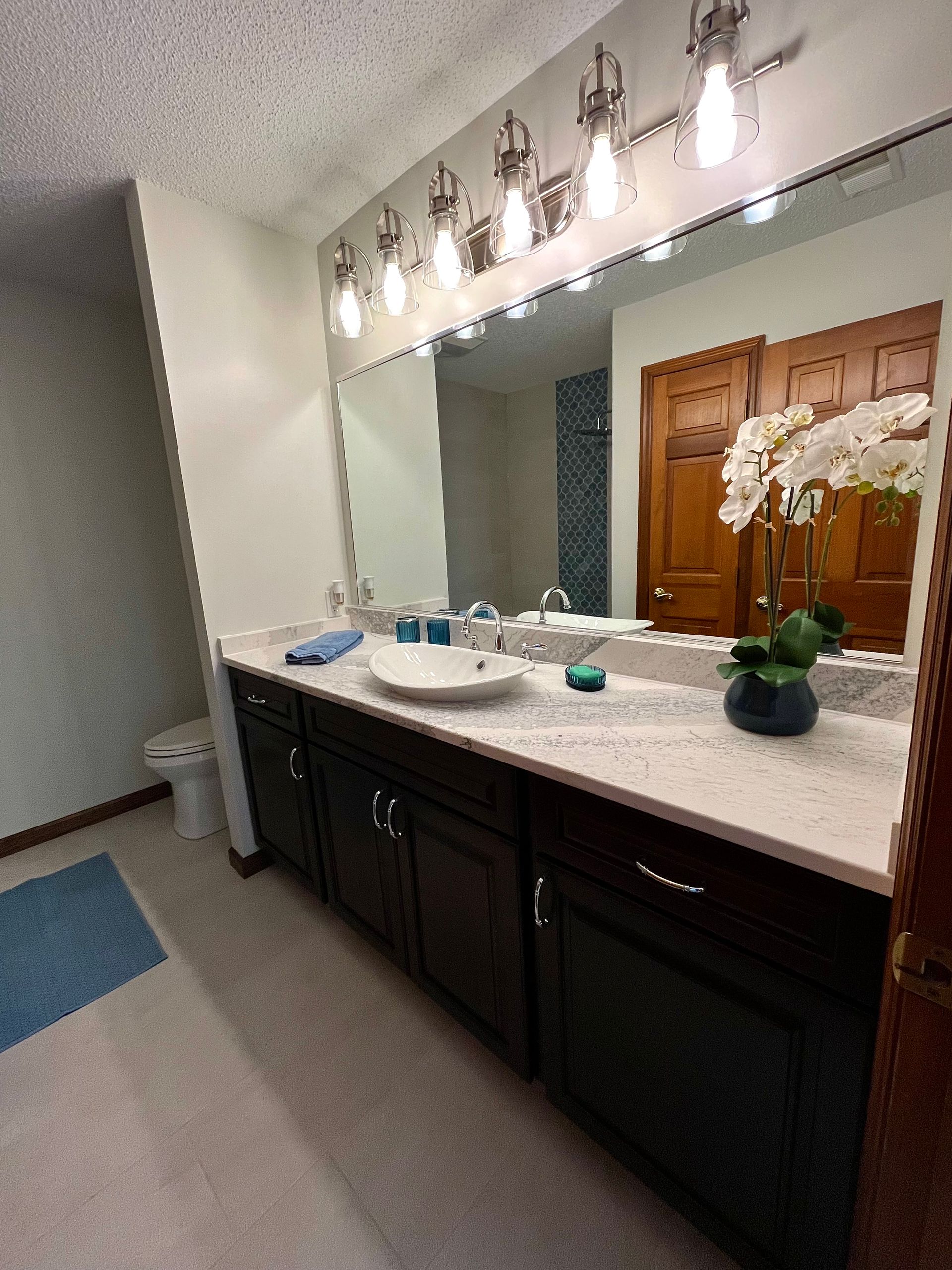 Bathroom with a large mirror, dark brown cabinets, and a white countertop.
