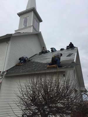 Roofers working on a white church roof with steeple under overcast sky.