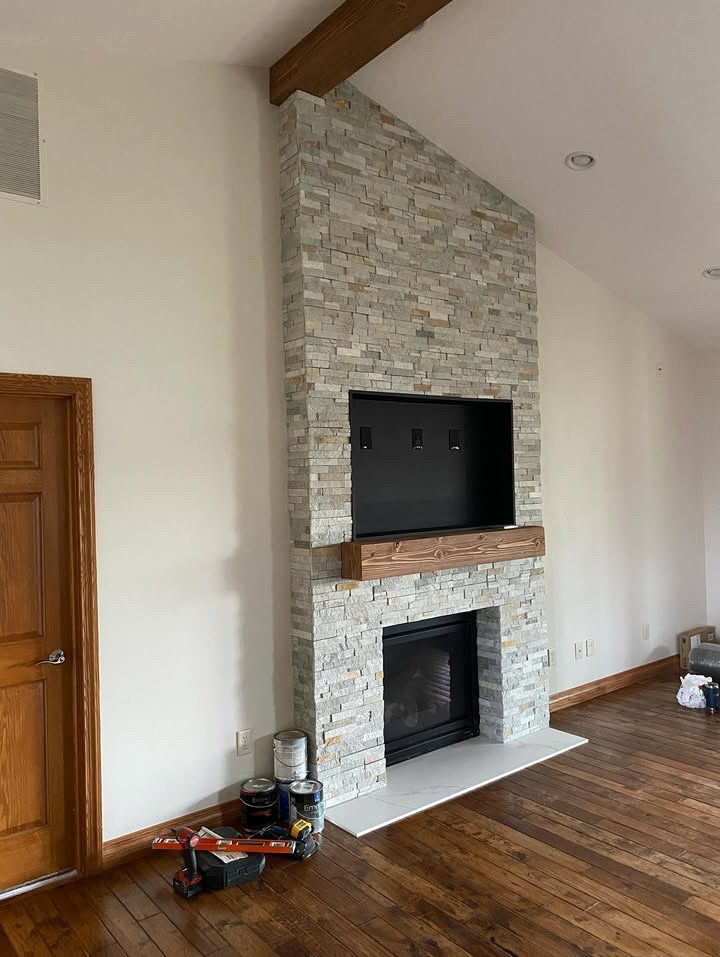 Fireplace with stone facade and built-in television against white walls and wood floor.