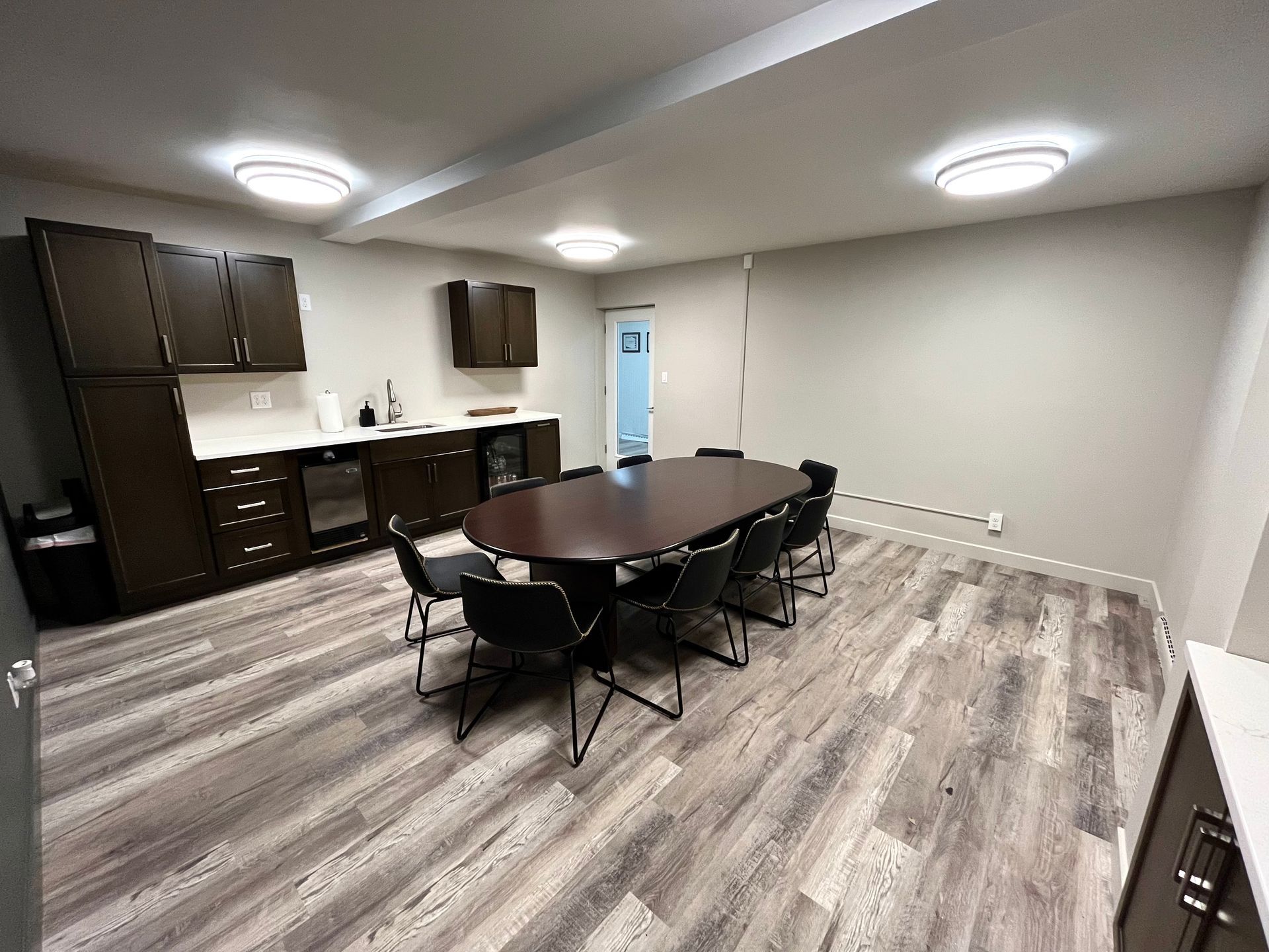 Meeting room with large oval table and chairs, built-in cabinets and counter, and wood-look flooring.