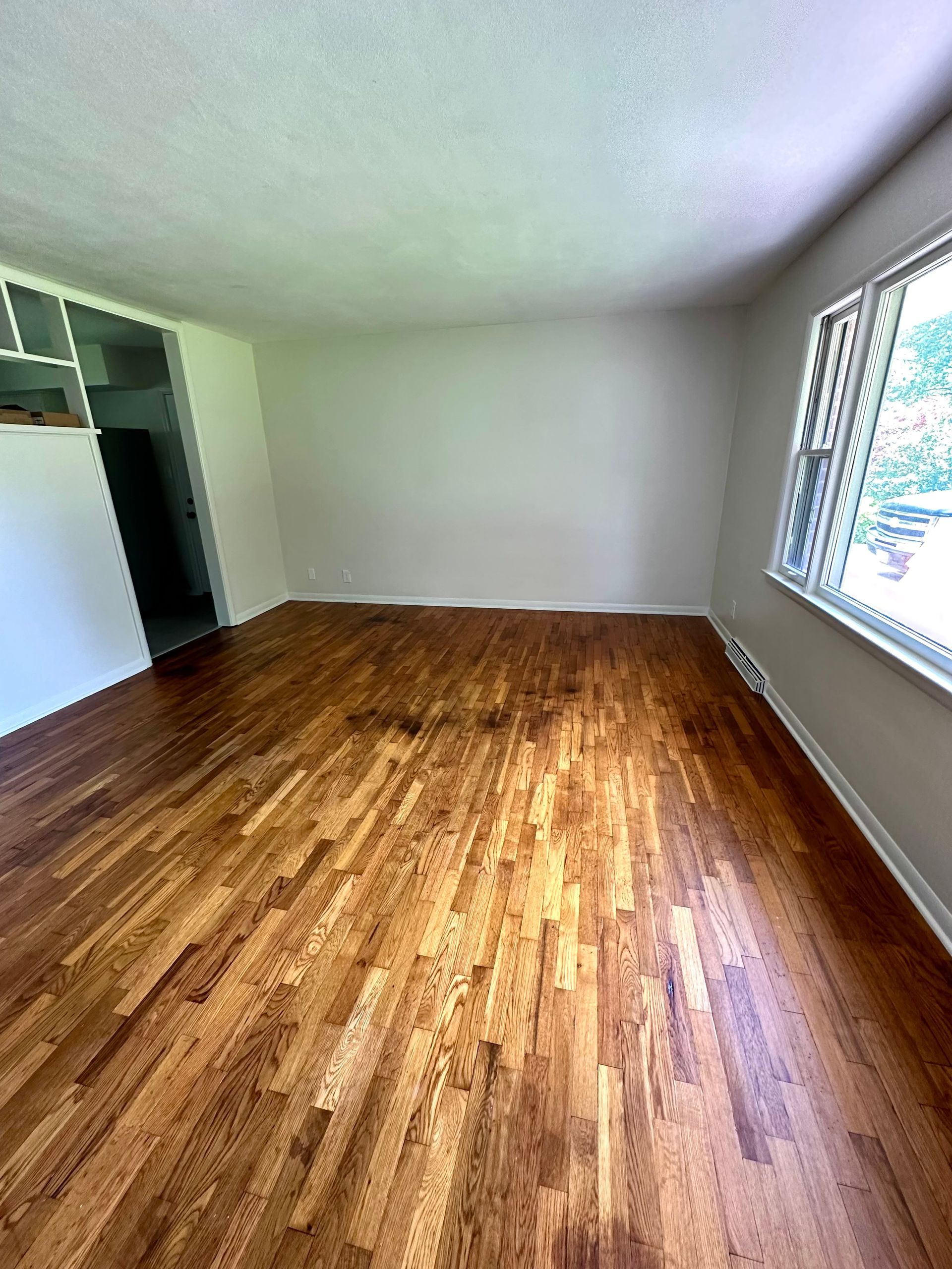 Empty room with hardwood floors, white walls, and a window.
