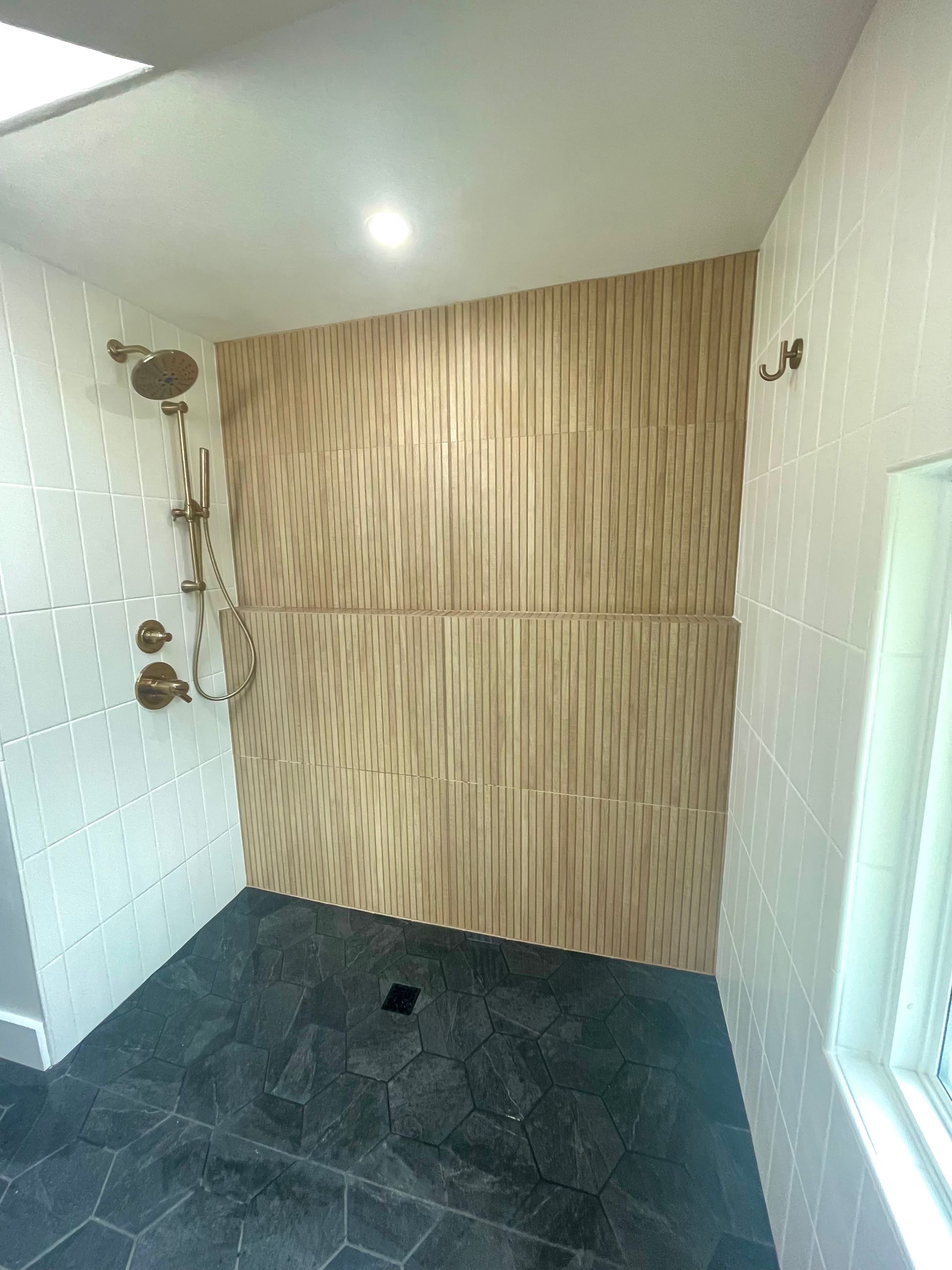 Modern shower with textured wood-look tile feature wall, bronze fixtures, white tile, and dark floor.