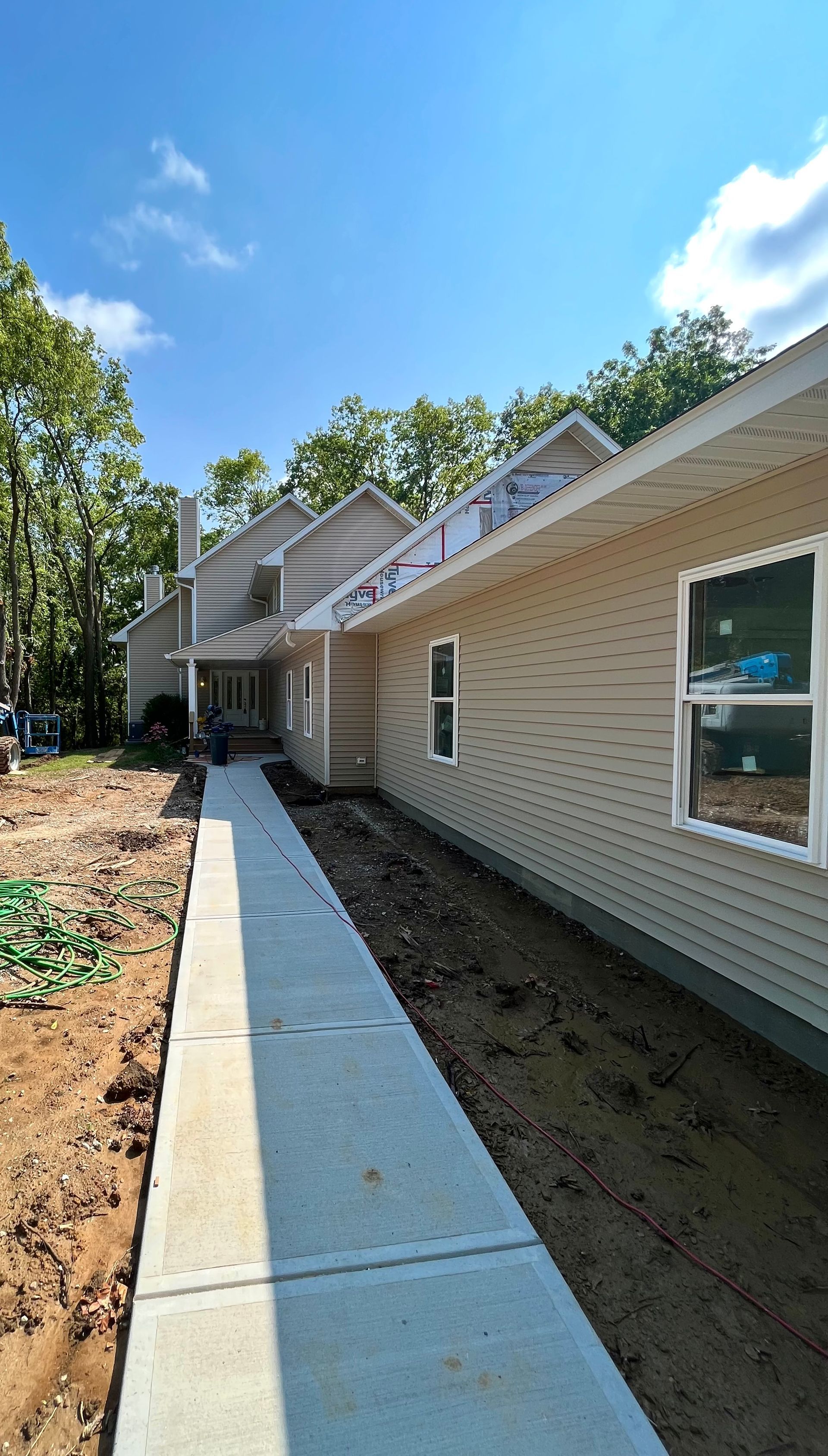 Beige house under construction, with a concrete pathway and blue sky.