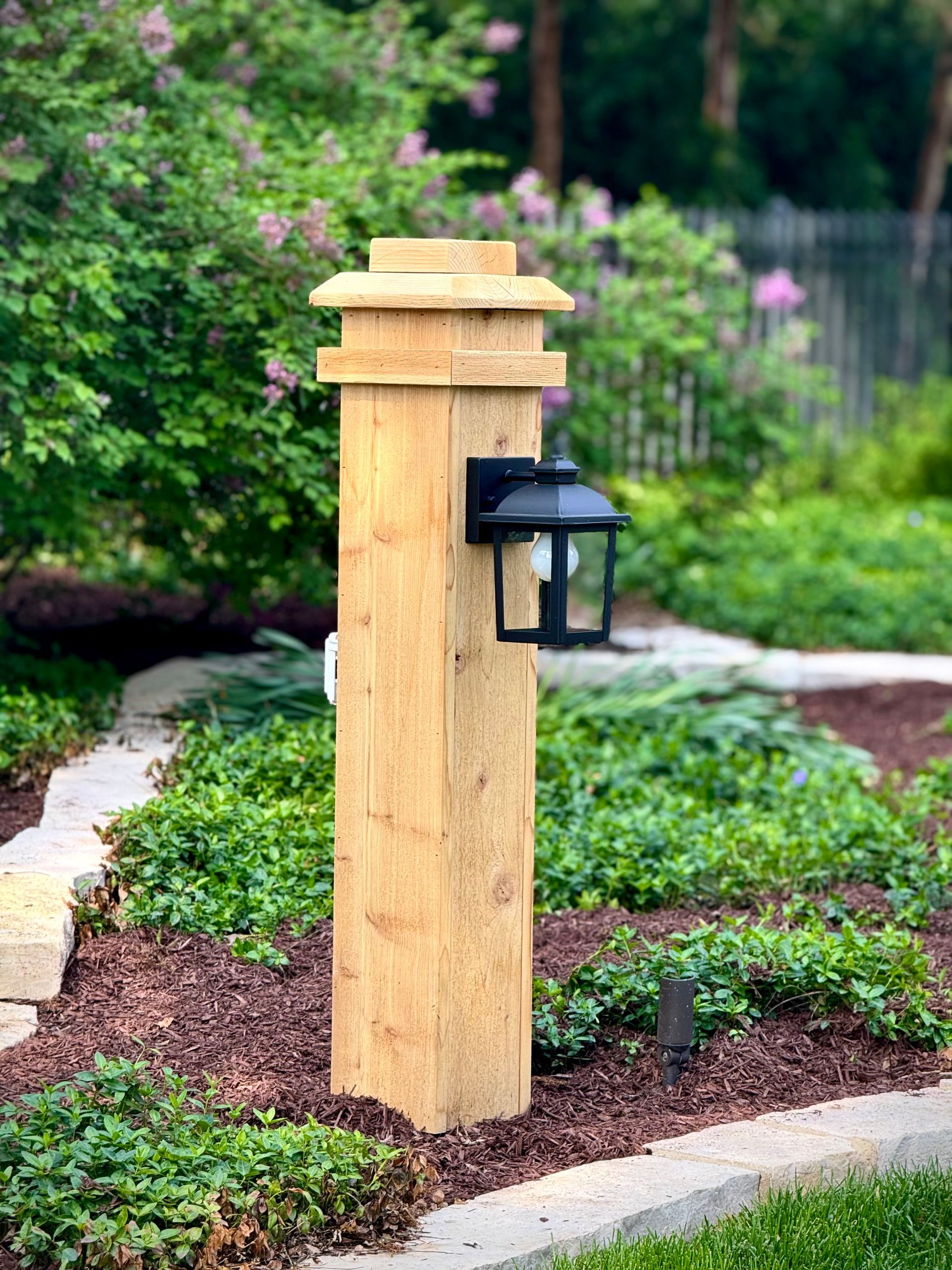 Wooden post with lantern in garden bed.