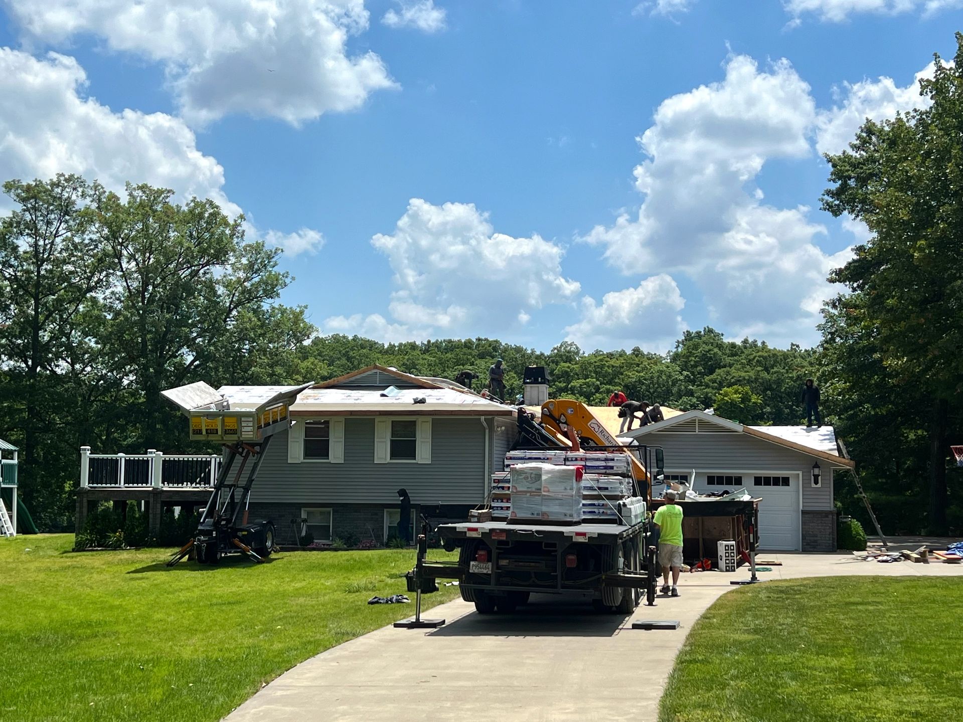 Roofing work in progress on a residential house and garage; truck with materials parked in the driveway.