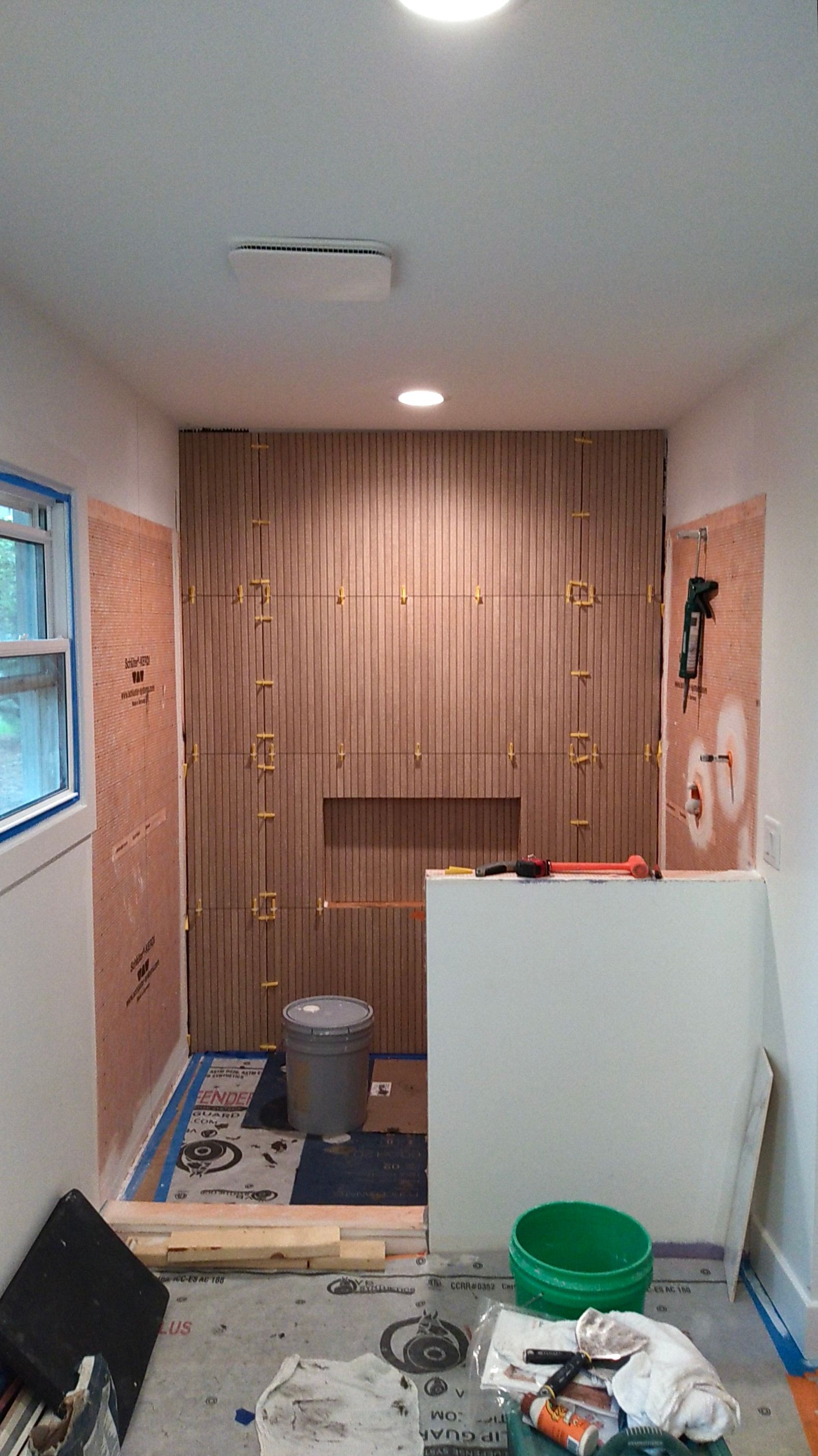 Bathroom remodel in progress; wood-paneled wall, plywood walls, tools, and materials are visible.
