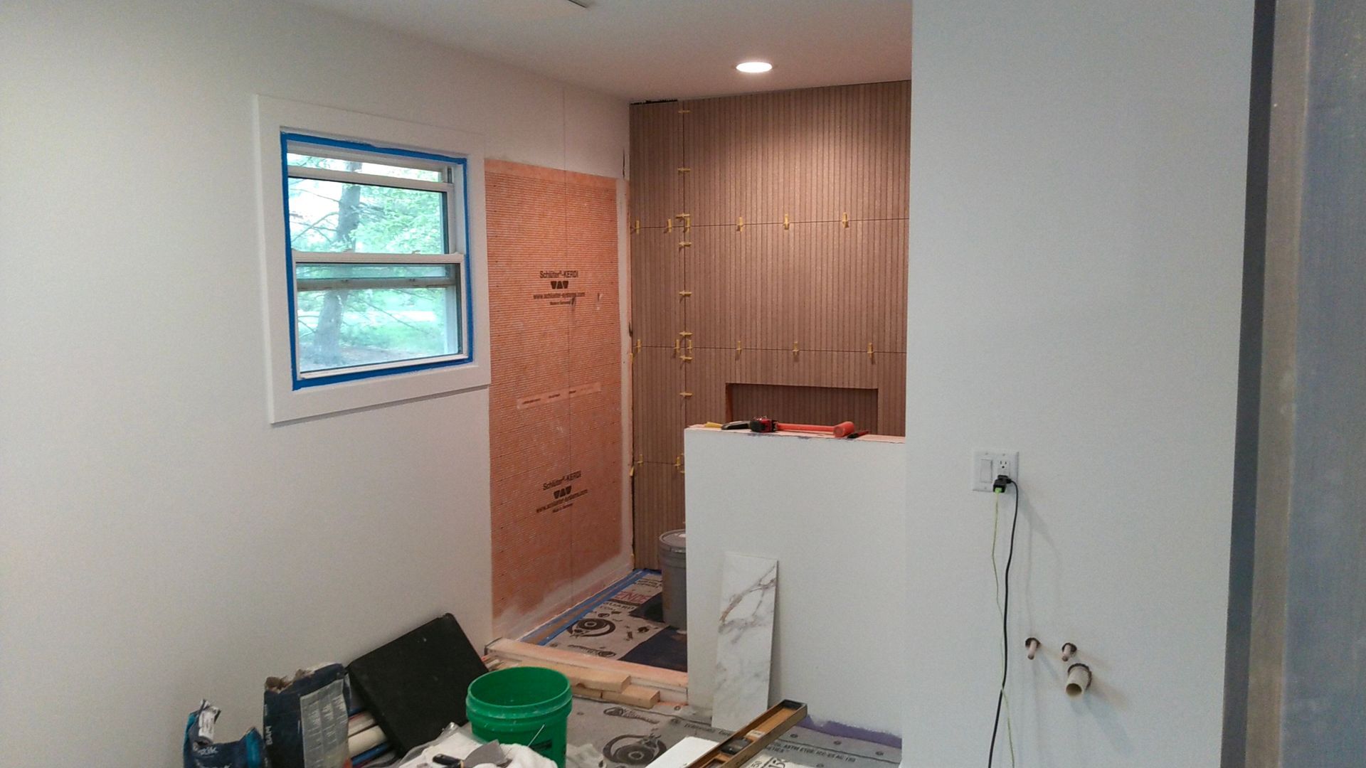 Bathroom under construction; white walls, small window, wood-paneled shower area, construction materials visible.