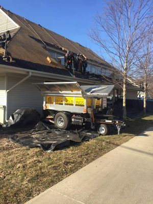 Roofers working on a building with a trailer for materials parked on the grass; sunny day.