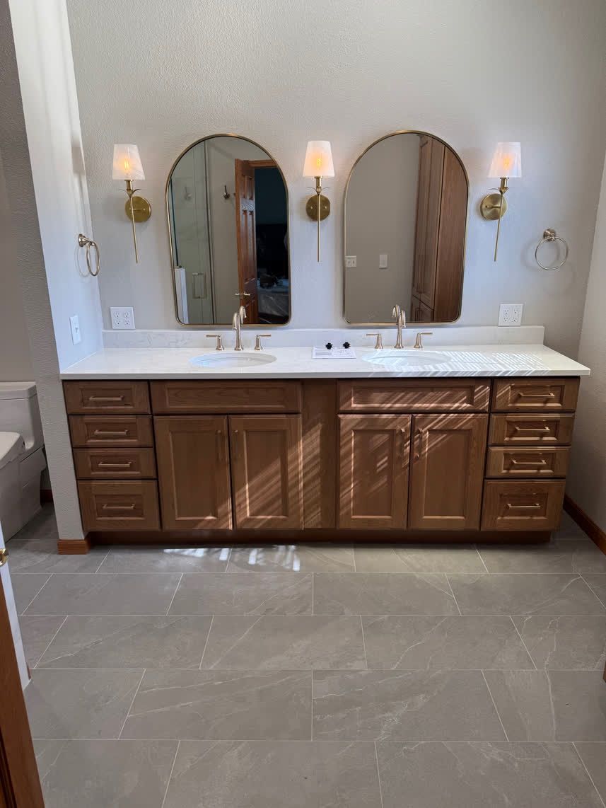Bathroom with a wooden vanity, two arched mirrors, and gold sconces.