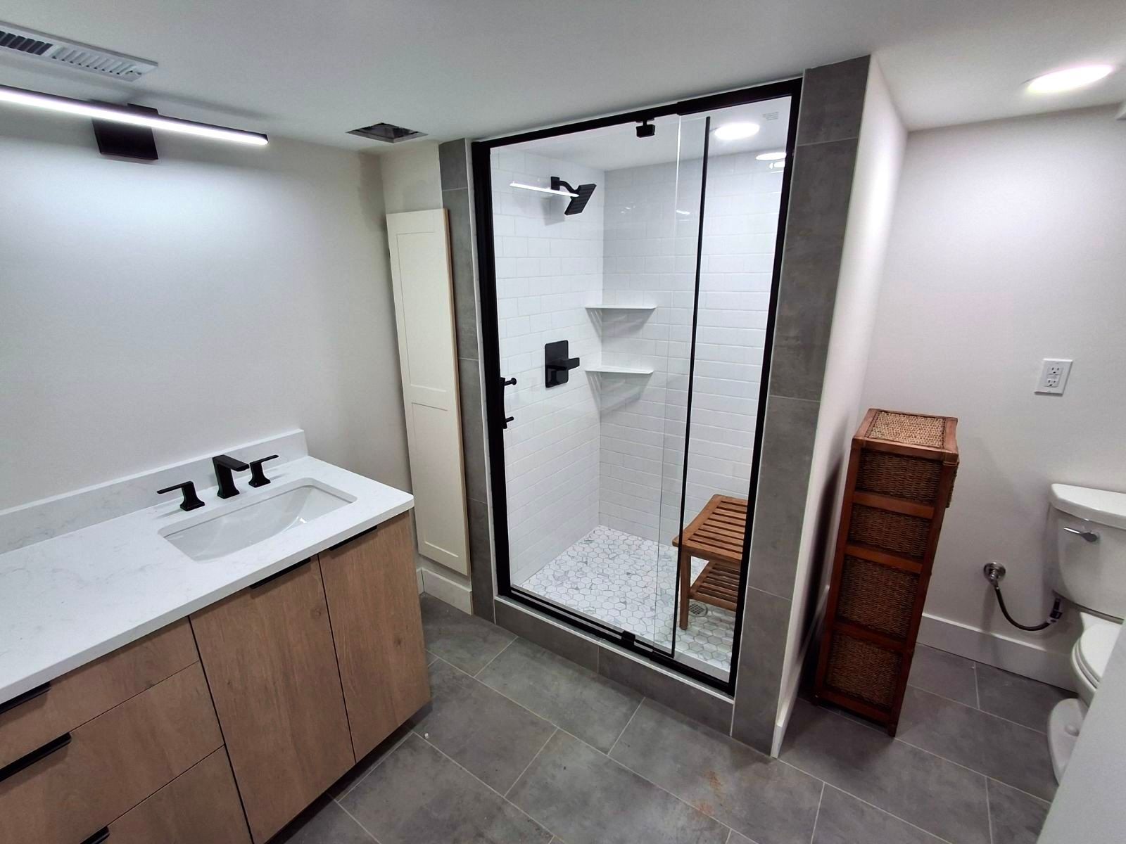 Modern bathroom with a glass-enclosed shower, wood vanity, and a wicker cabinet.