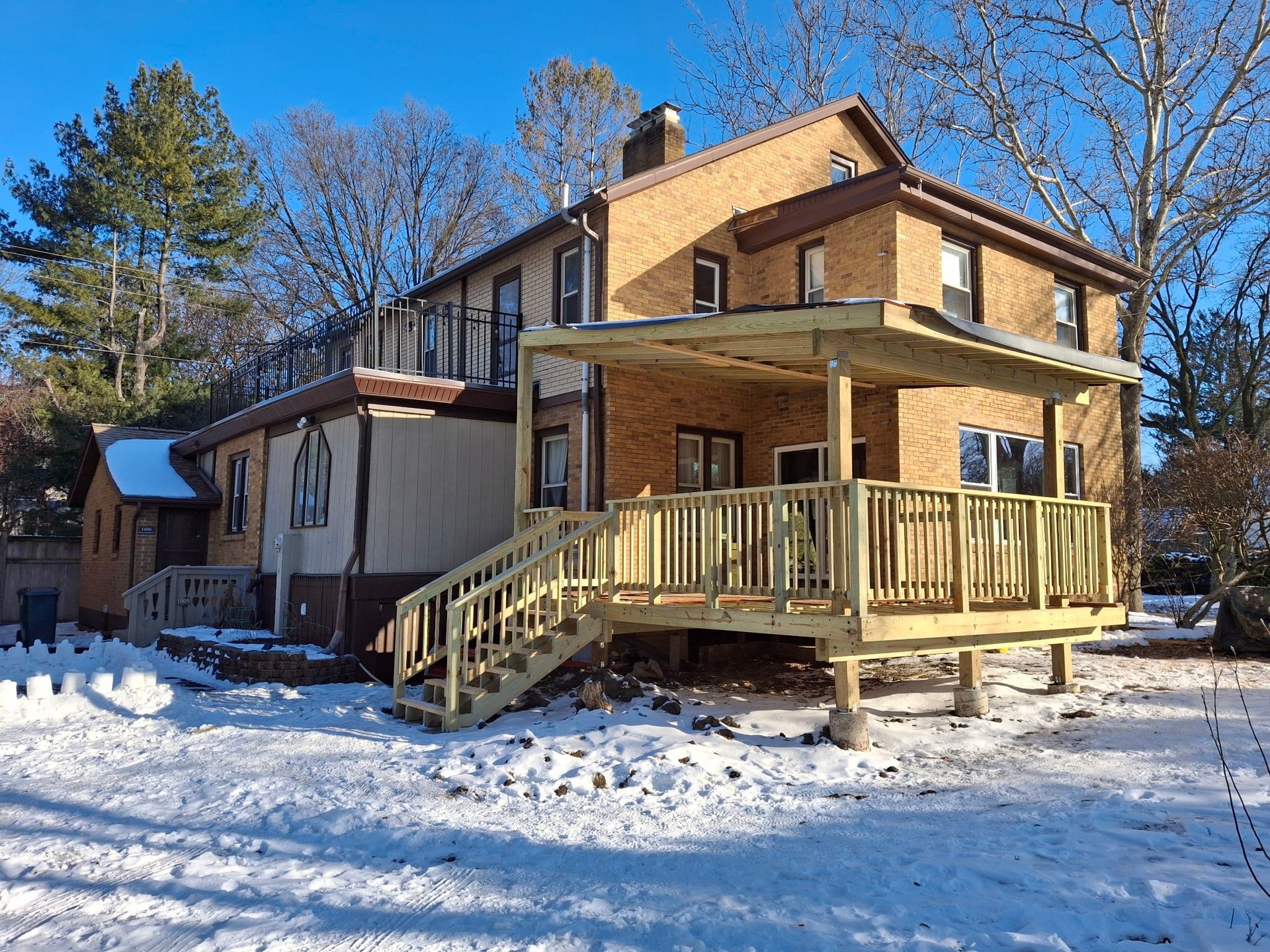Back view of a two-story brick house with a newly constructed wooden deck and snow on the ground.