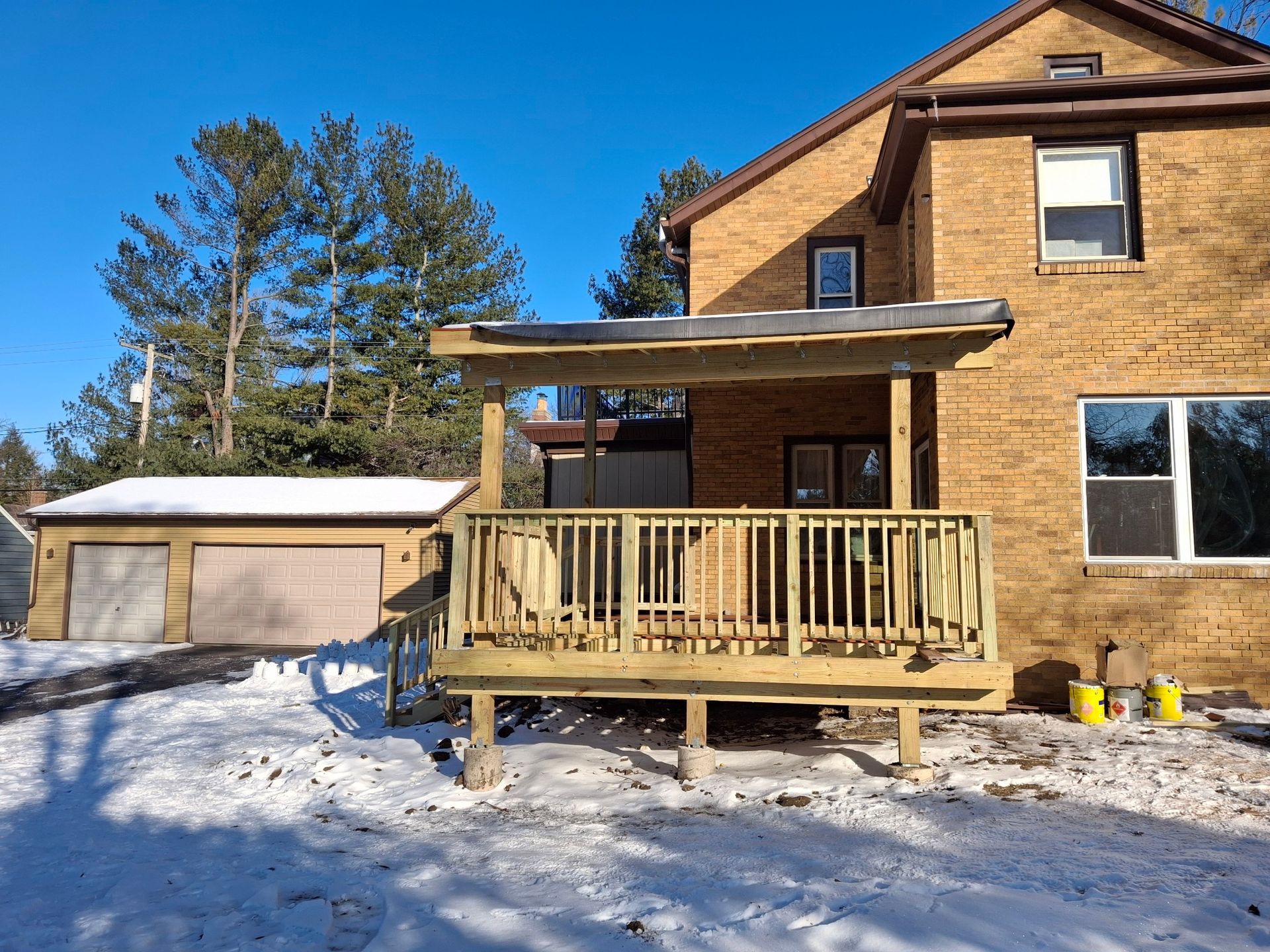 Wooden deck attached to a two-story brick house, with a garage in the snowy background.