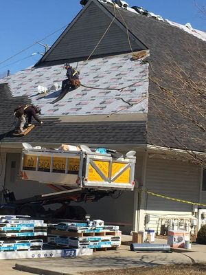 Roofers working on a house, materials on a lift, blue and gray shingles, clear sunny day.