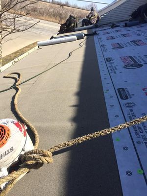 Roofers working on a black roof, roped down, tools nearby. Sunny day, residential setting.