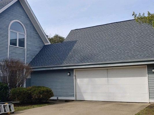 Blue house with gray shingle roof and white garage door. Overcast sky.