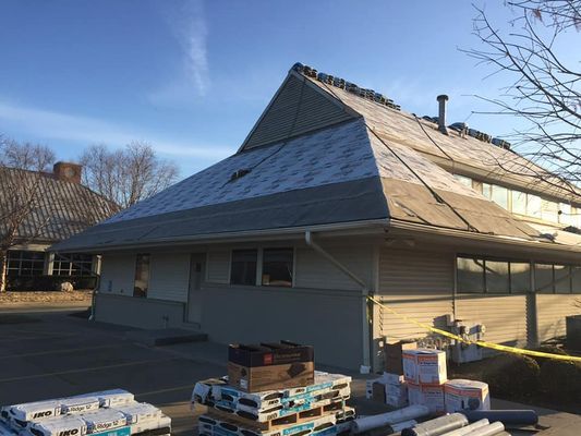 Building with a damaged roof, materials on the ground, and a sunny sky.