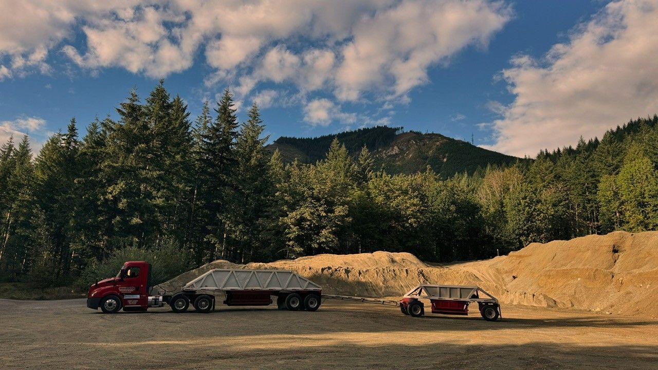 A red semi truck is towing a car in a parking lot.
