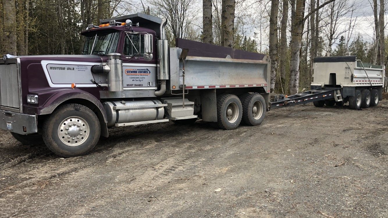 A dump truck is parked in a gravel lot next to a trailer.