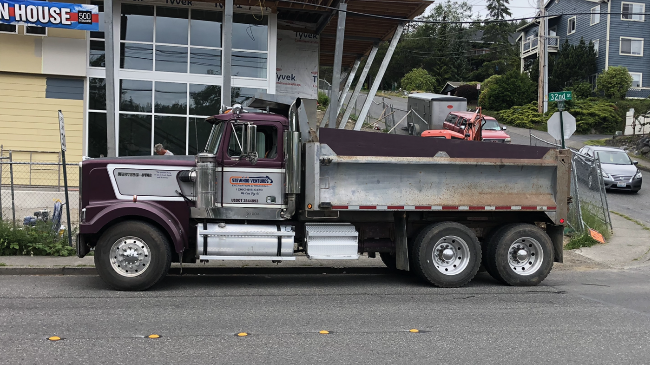 A dump truck is parked on the side of the road in front of a building.