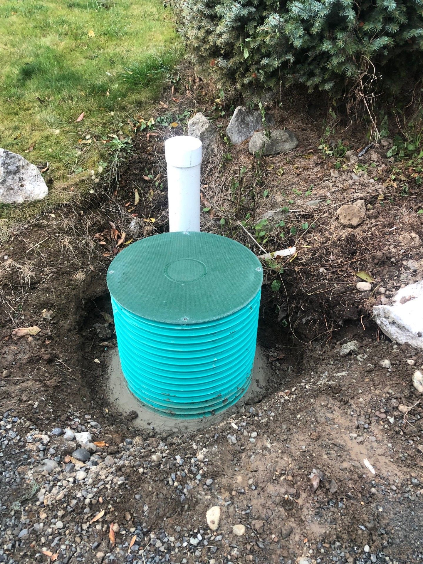 A green barrel is sitting in the dirt next to a white pipe.